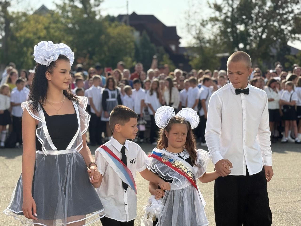 Одиннадцатиклассники ведут первоклассников за руку на торжественную линейку..